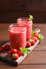 Glass jars with tasty strawberry smoothie on wooden table