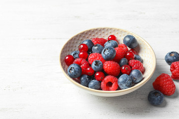 Bowl with raspberries, red currant and blueberries on wooden table