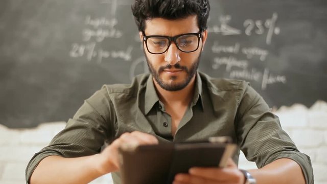 Smiling male teacher using tablet as having a break, searching interesting resources online while preparing for classes, concept of importance of technology in every occupation