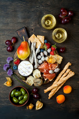 Fototapeta na wymiar Appetizers table with italian antipasti snacks and wine in glasses. Cheese and charcuterie variety board over rustic wooden background