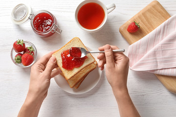 Woman spreading strawberry jam on toast bread over table