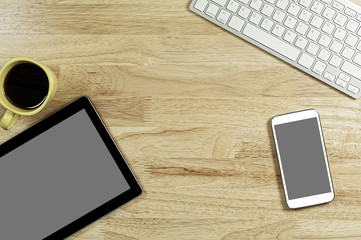 blank screen smartphones and tablet PC on the wooden desktop with computer keyboard and a cup of coffee in composition with copy space for your text
