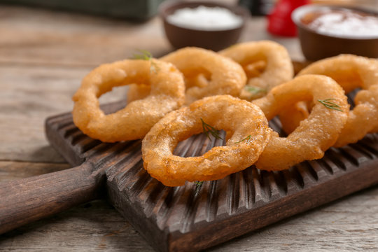 Wooden board with fried onion rings on table, closeup