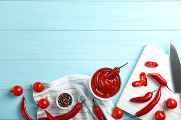 Flat lay composition with bowl of hot chili sauce on wooden background