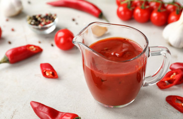 Jug with spicy chili sauce on light table