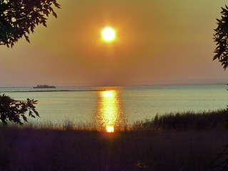 A picturesque sunset of a bright summer sun over a transparent water surface
