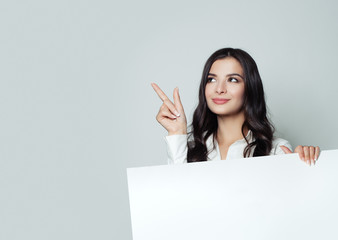 Happy young businesswoman pointing up and showing signboard with blank copy space area for tagline,...