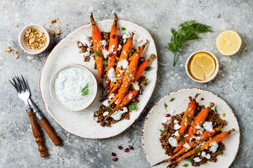 Roasted carrots lentil salad with feta, herb yogurt and dukkah on a light concrete background....