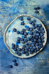 Fresh blueberries on the vintage ceramic plate over blue background. Top view, flat lay. Healthy eating concept.