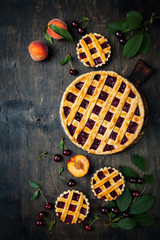 Homemade cherry pie on rustic background with cherries and peaches