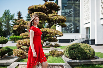 Teenage girl in red dress posed outdoor at sunny day.