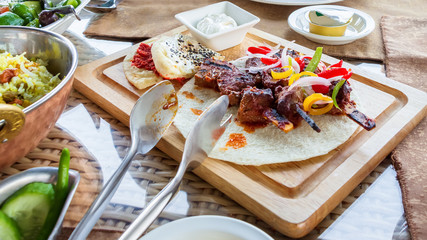 Barbecue grill meat served with vegetables tortilla and sauce on wooden cutting board. Served lunch.