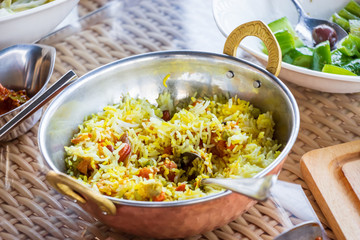 Closeup spicy and delicious chicken biryani served with sauce raita and achar. Served in authentic indian copper utensils.