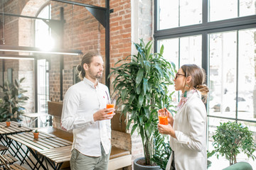 Young couple dressed in white standing together with drinks during the conversation in the...