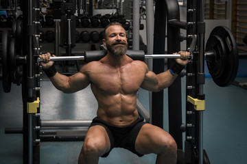 Fototapeta na wymiar Hombre fuerte con grandes músculos haciendo sentadillas mientras entrena en el gimnasio. Ponerse en forma.