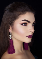 Fototapeta premium Beautiful brunette with long earrings on a black background.