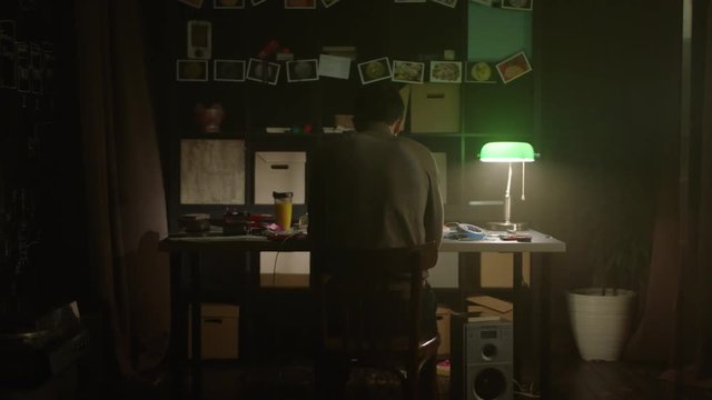 Tired young man working with laptop at home in evening. Stock. Sad lonely man sitting at the table at home. The concept of loneliness