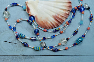 Long beads of glass and seashells on a wooden blue table. Composition with female glass jewelery from Murano.