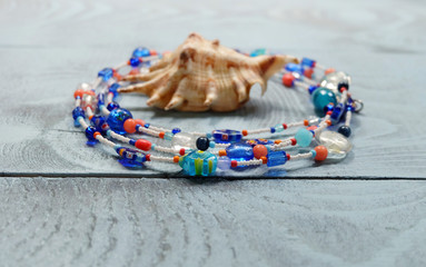 Long beads of glass and seashells on a wooden blue table. Composition with female glass jewelery from Murano.