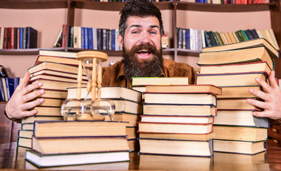 Man on happy face between piles of books, while studying in library, bookshelves on background....