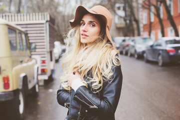 Obraz premium lifestyle portrait of young beautiful woman walking outdoor on city streets, wearing hat and leather jacket. Real people, candid shot.