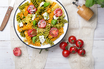 Włoskie jedzenie - Sałatka z kolorowym makaronem, pomidorami koktajlowymi, serem feta i świeża bazylią na białym drewnianym tle.   © czarny_bez