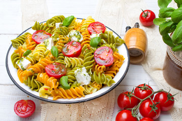 Italian food - Salad with colorful pasta, cherry tomatoes, feta cheese and fresh basil on white wooden background