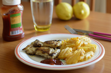 Primer plano de un plato de contramuslos de pollo a la plancha con patatas y ketchup en una mesa de madera