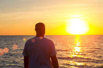 a man stands with his back looking at the sea and the sunset - Powered by Adobe