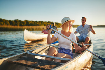 Laughing young woman canoeing on a lake with friends - obrazy, fototapety, plakaty
