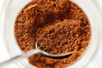 Ground natural coffee inside of glass jar with metal spoon, macro