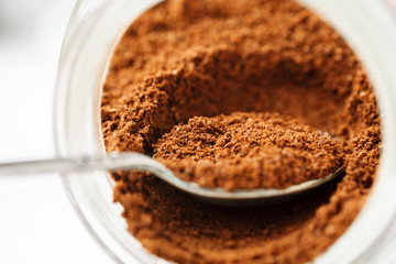 Ground natural coffee inside of glass jar with metal spoon, macro