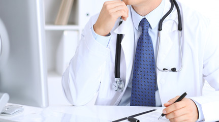 Unknown male doctor is sitting at the table and working in the hospital office. Closeup of stethoscope