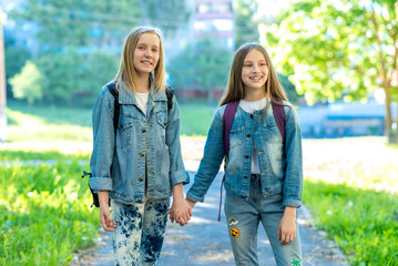 Two girls schoolgirl. Summer in nature. They hold each other's hands. The concept best friends. Returns home after school. Smiles happily.