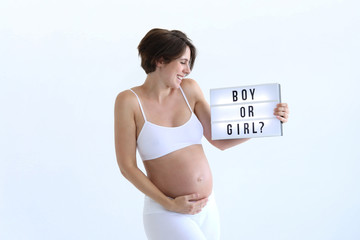 Hübsche schwangere Frau hält lachend ein Schild in die Höhe mit der Frage boy or girl