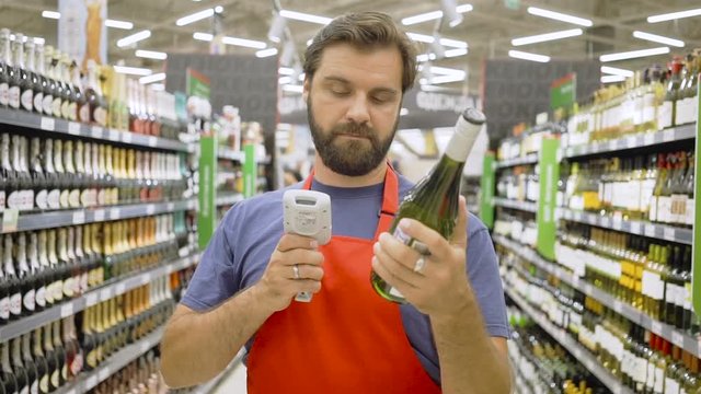 supermarket employee in red aport scanning bottle barcode at wine section in supermarket