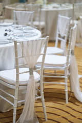 Back of white chiavari chairs decorated with white sash organza stripe for wedding reception party dinner table