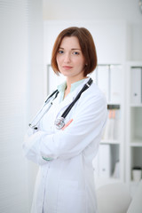 Young brunette female doctor standing with clipboard and smiling in hospital