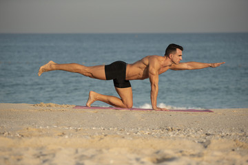 Fototapeta na wymiar A handsome muscular caucasian white European male performs a yoga exercise pose on the beach on a summer morning. 