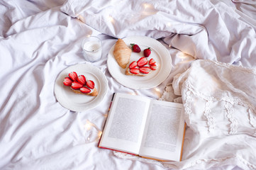 Tasty breakfast with strawberry cake and book in bed close up. Good morning. Selective focus.