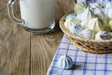 Meringues in a plate and with a cup of milk on a wooden table
