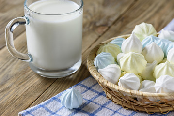 Colorful meringues in a plate and with a cup of milk on a wooden table