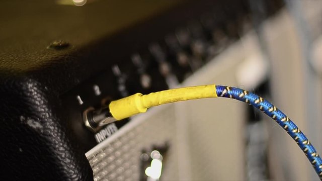 Hands plugging guitar to electric amplifier.