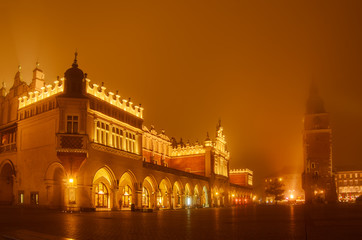 Fototapeta na wymiar Market hall and town vity hall at main Cracow square at misty night with golden sky
