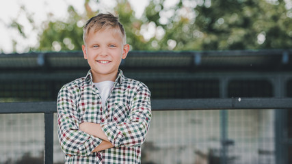 happy boy in checkered shirt standing with crossed arms and smiling at camera on farm