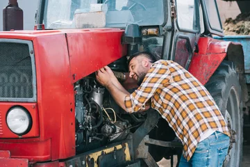 Photo sur Plexiglas Tracteur handsome middle aged farmer in checkered shirt repairing tractor