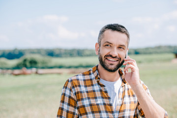 smiling middle aged farmer talking by smartphone in field