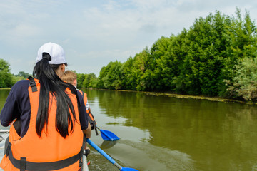 Brunette in a white cap and a life jacket on a catamaran rowing an oar