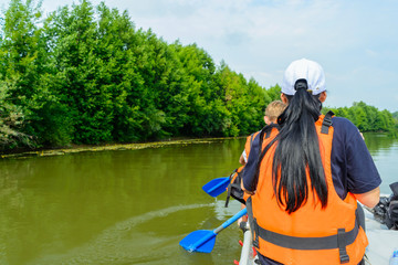 A woman in a cap and an orange life jacket works as a paddle on an inflatable catamaran