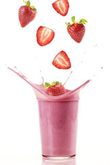 Delicious strawberries falling into a glass of strawberry milkshake / Fresh strawberries falling into a glass to make a delicious strawberry smoothie. White background.